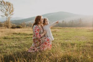 Mother and child sitting in golden sunlit field with mountains visible in distance.