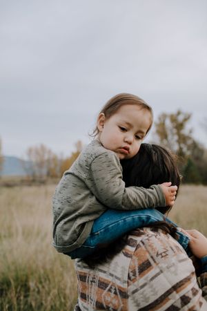 A tender embrace between parent and child in a serene field with mountains in the background.