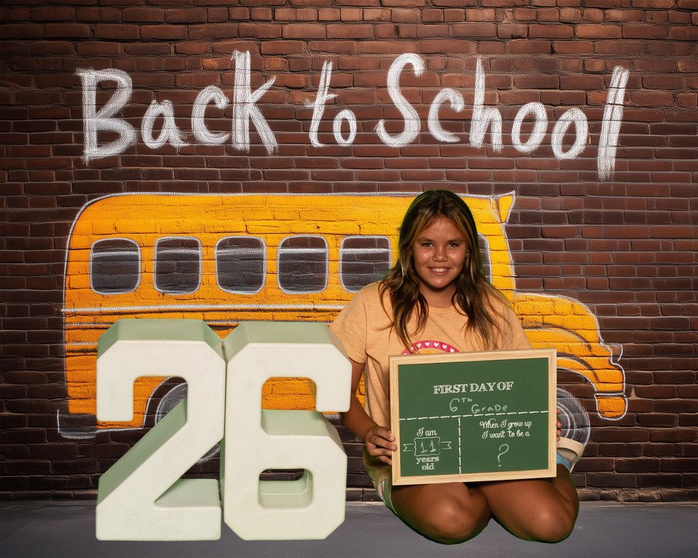 School themed photo with chalkboard and decorative yellow bus against brick wall displaying Back to School text.