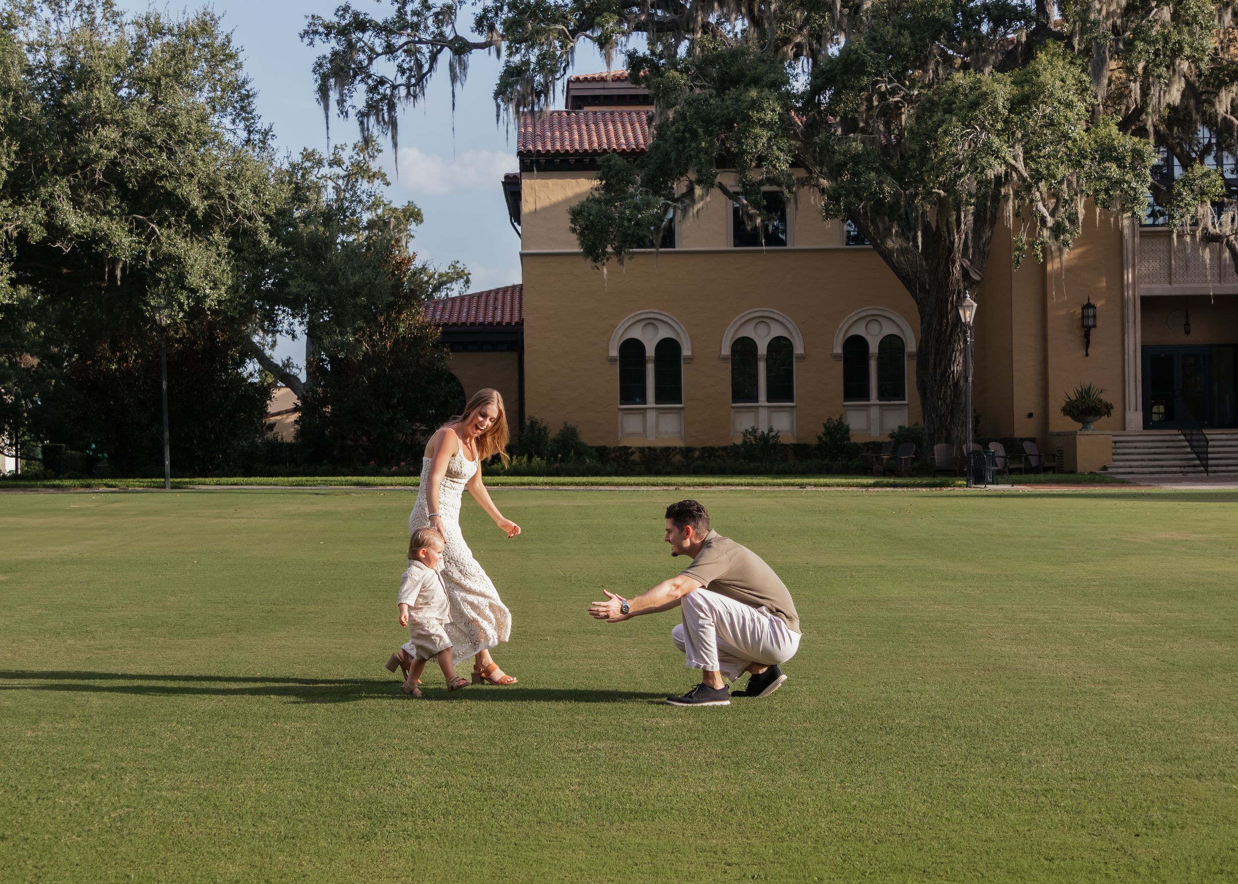 People play and interact on vast green lawn with Spanish-style building in background.