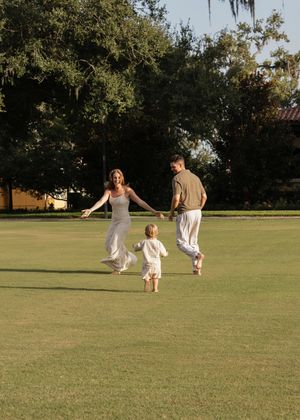 Family members spread out across a sunny lawn playing together in white summer outfits.