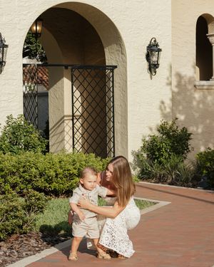 Family plays together on brick pathway near cream colored building with arches.