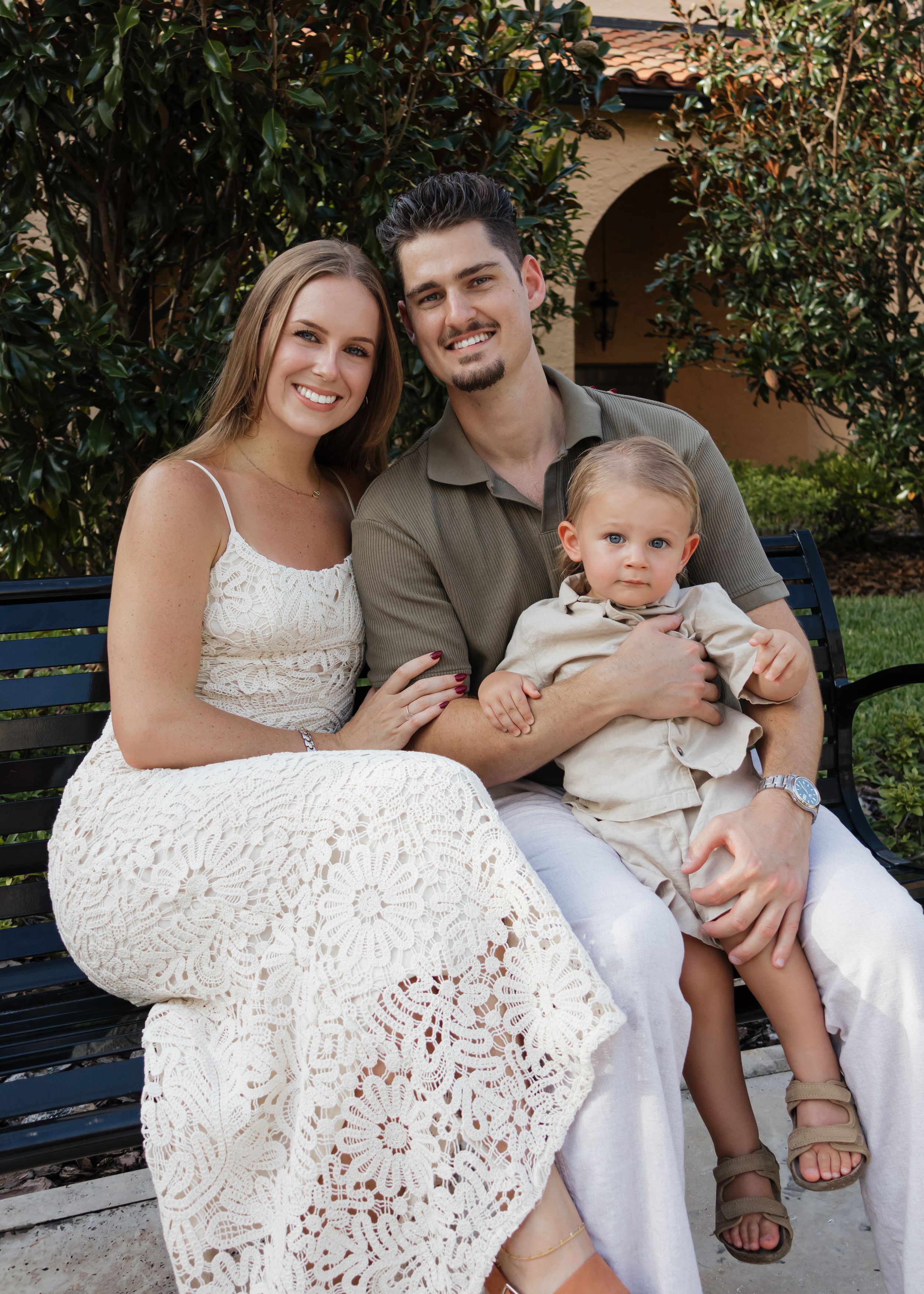 Family sits together on a bench wearing coordinated white and olive green outfits.