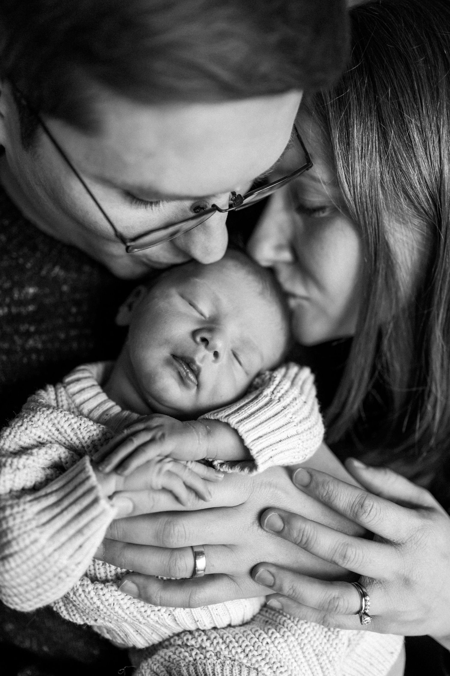 An intimate black and white family portrait showing gentle affection with their sleeping baby.