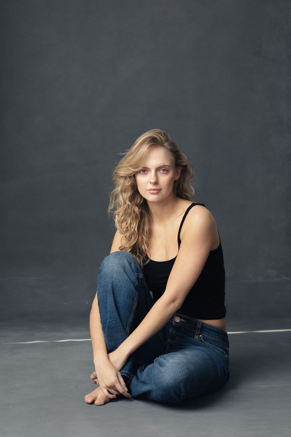 Casual portrait in black top and jeans against dark studio background.