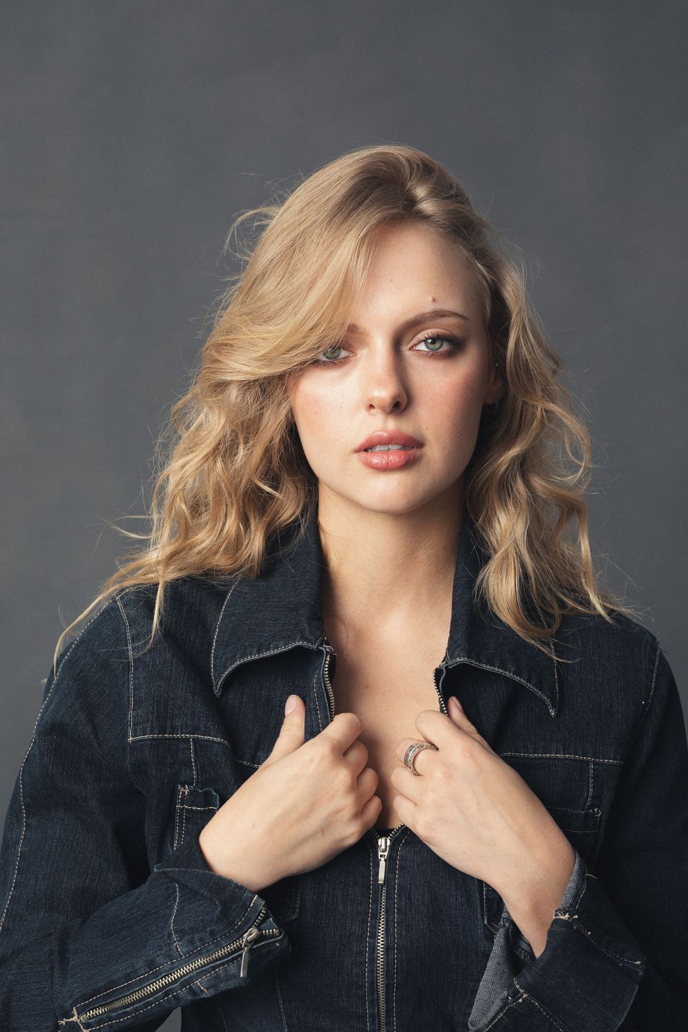 Fashion model wearing black denim jacket poses against gray backdrop in dynamic portrait series.