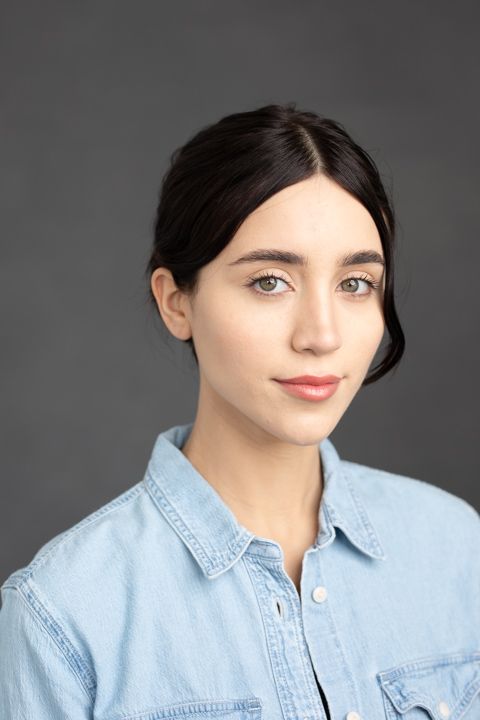 Headshot of woman wearing light denim shirt against dark background.