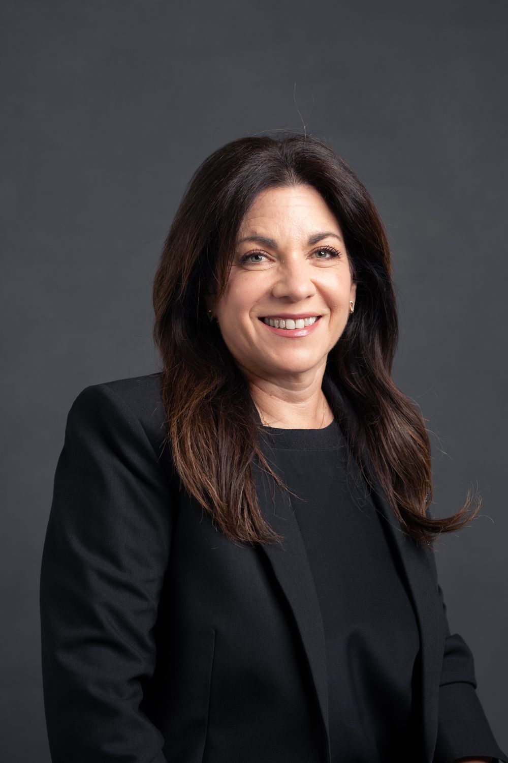 Professional headshot of woman in black blazer against dark background.
