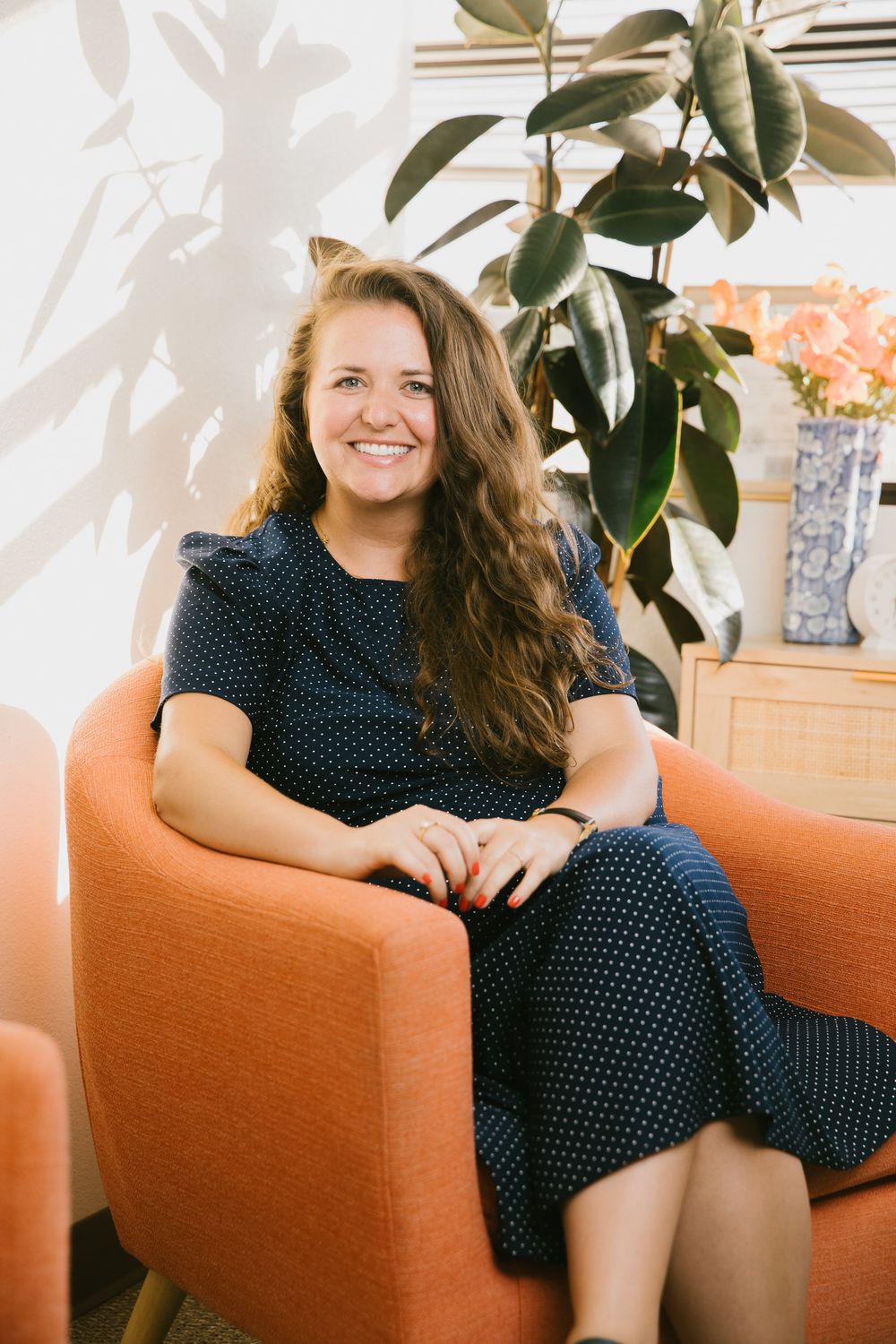 Woman relaxing on an orange couch with indoor plants in a bright modern space.