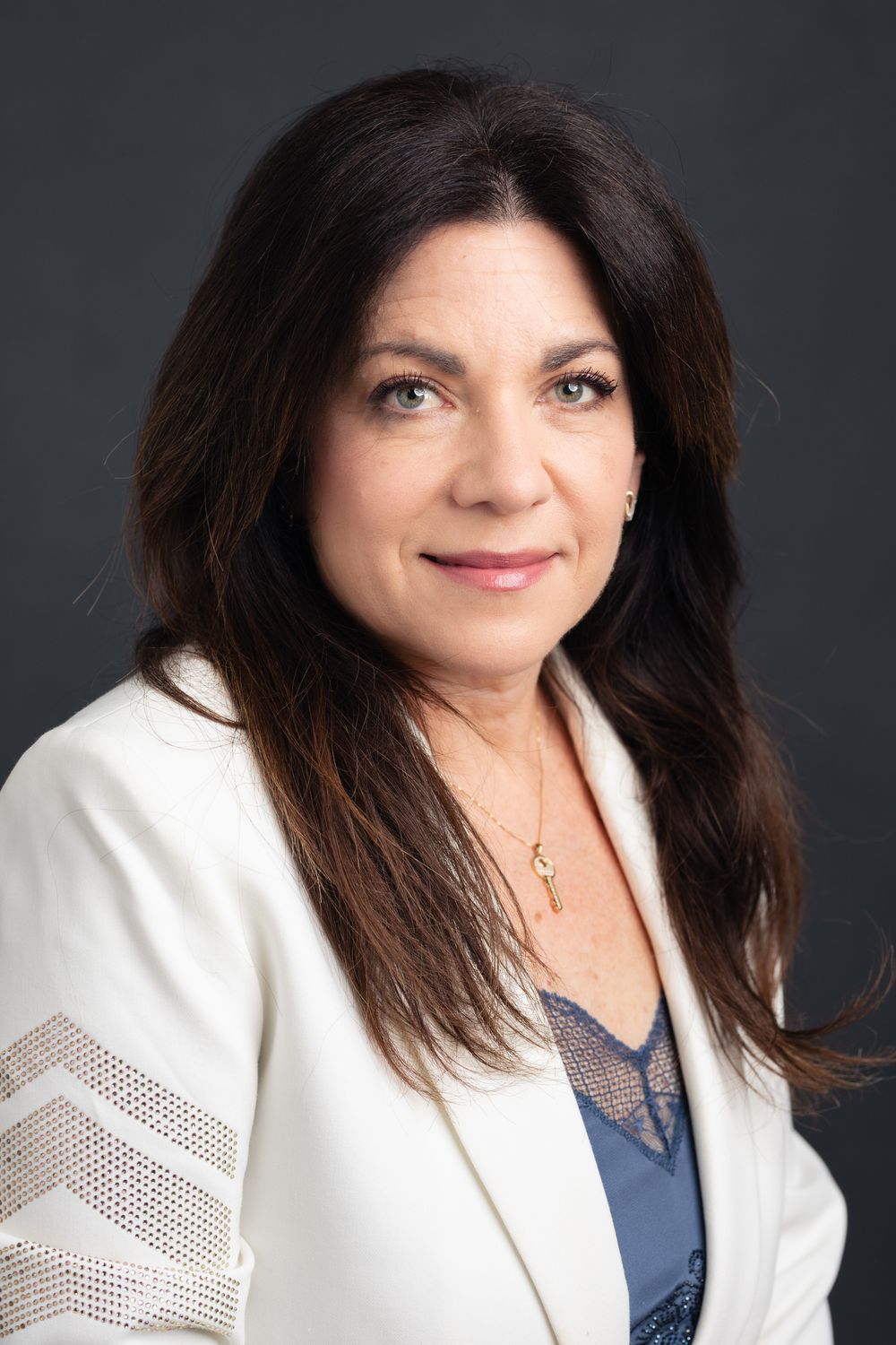 Professional portrait of a woman in a white blazer with lace detail against a dark background.