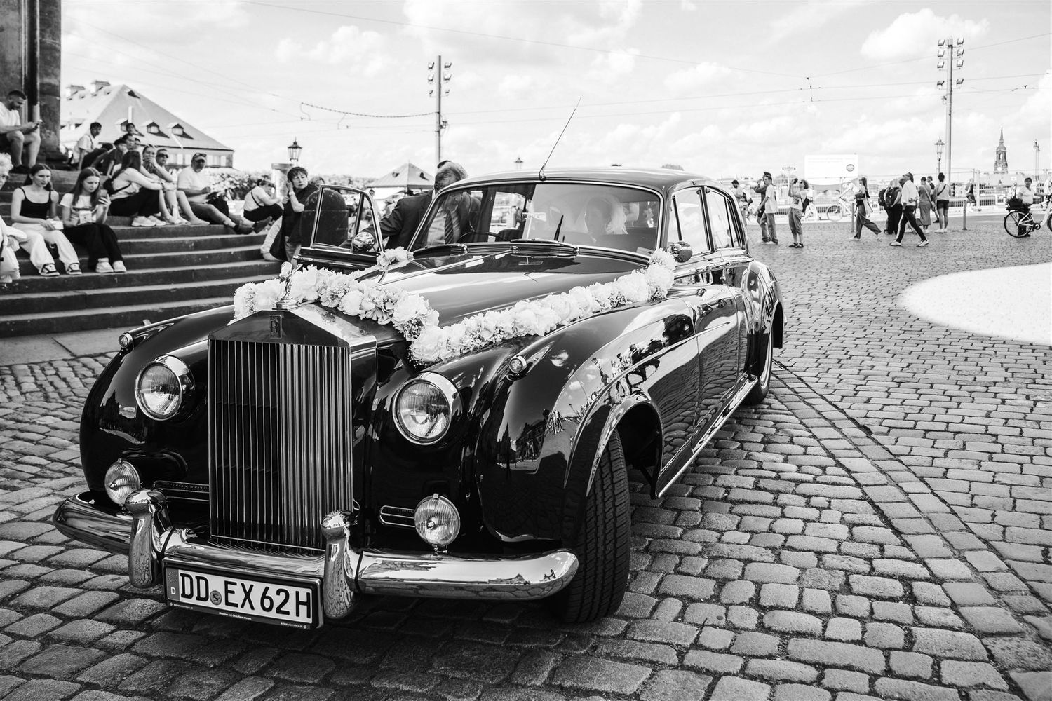A classic black Rolls Royce luxury car parked on cobblestone street in vintage black and white photograph.