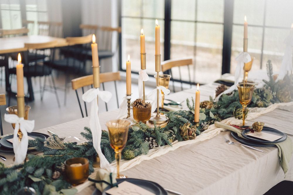 An elegant wedding table setting with white linens, greenery garlands, and golden candlesticks in a bright, airy venue.