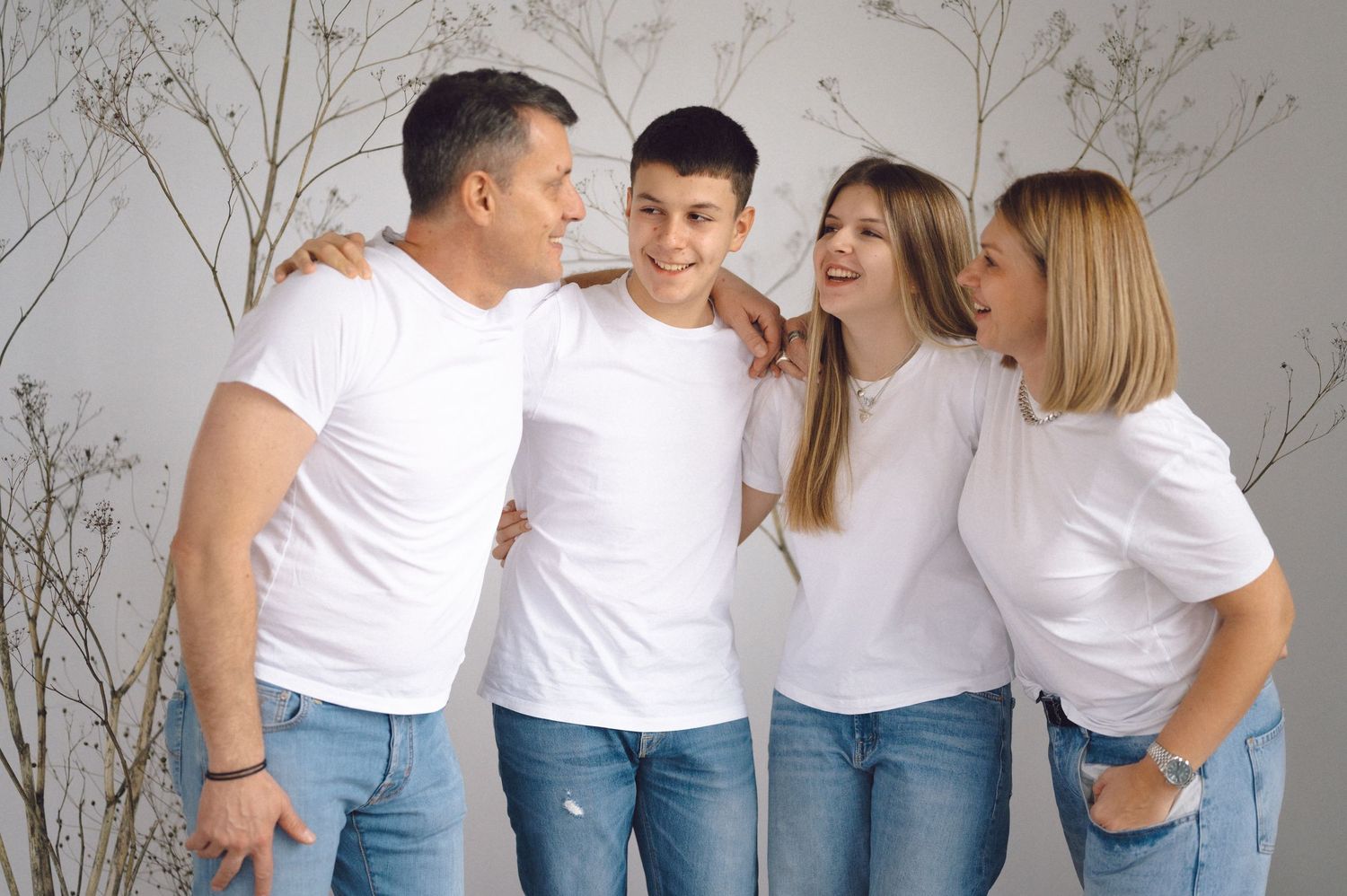 Group of people wearing matching white t-shirts and jeans pose together against light gray background.
