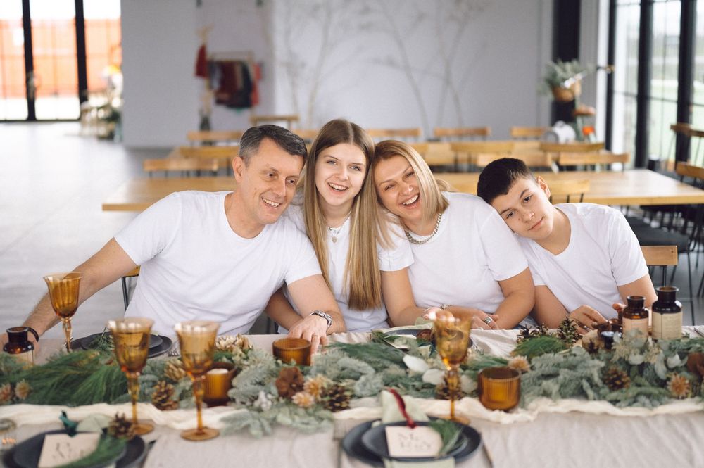 Happy group in white shirts gather around decorated table with amber glasses and greenery garland centerpiece.