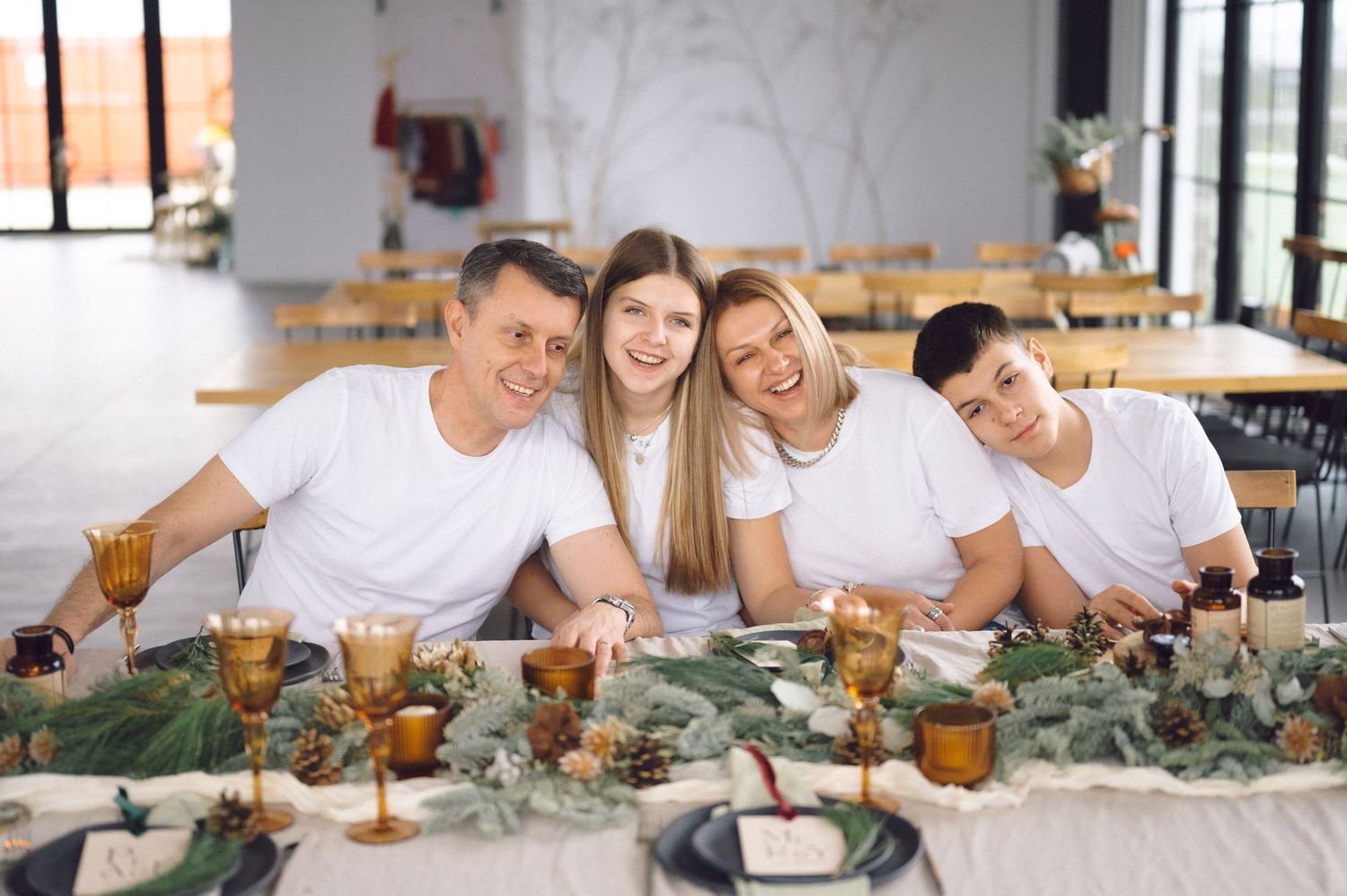 Happy group in white shirts gather around decorated table with amber glasses and greenery garland centerpiece.