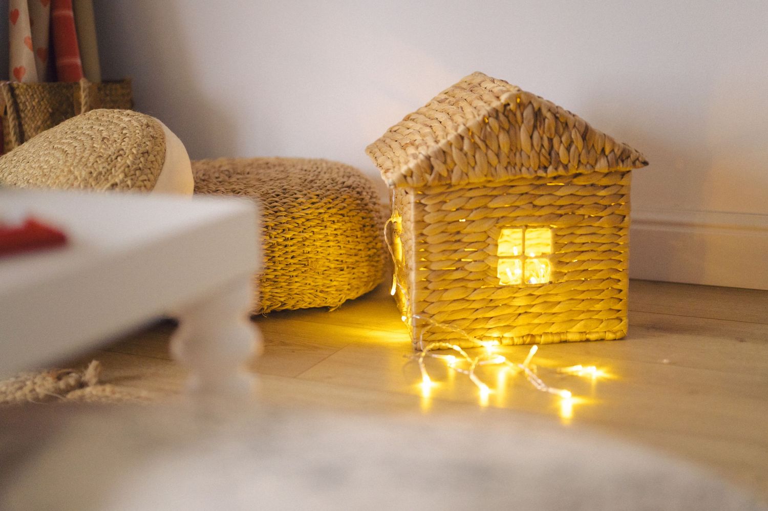 A cozy woven straw house decoration glows warmly with string lights inside on a light wooden floor.