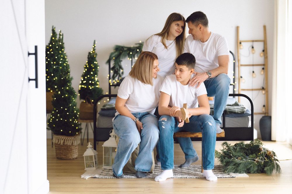 A family sits together at home during the holidays with a decorated Christmas tree in the background.
