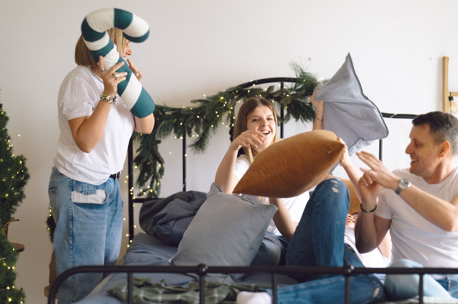 Friends having fun during playful pillow fight in bedroom with garland decoration.