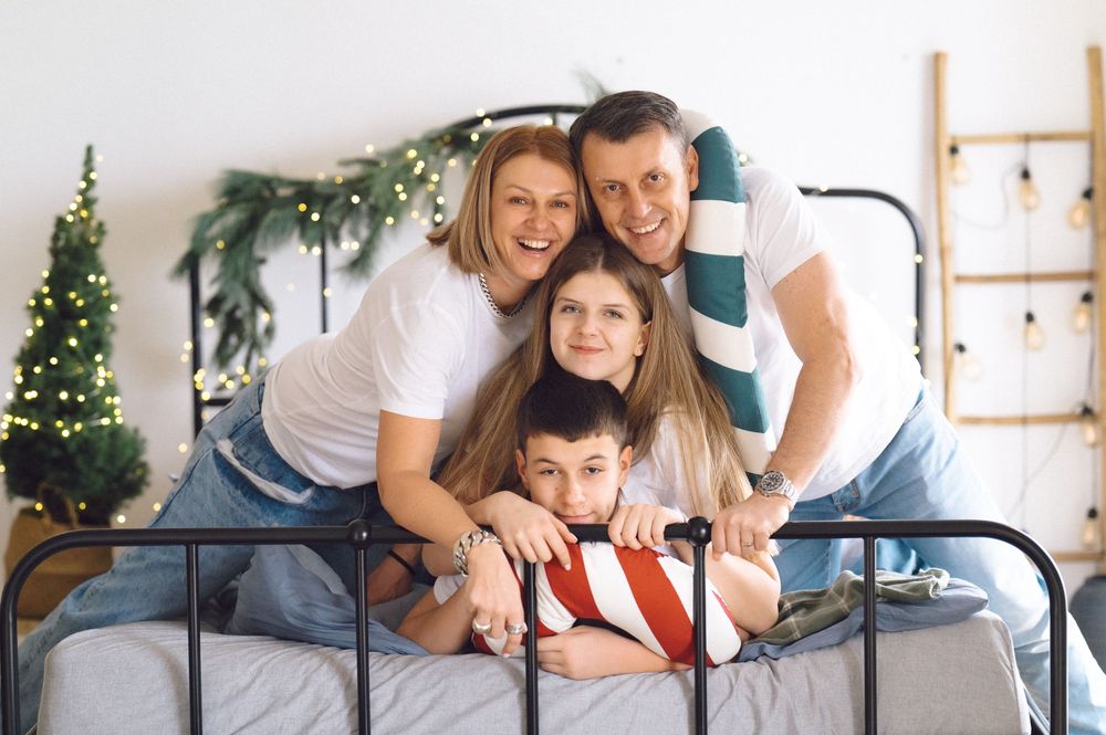 Family members relaxing together on gray sofa during winter holiday photoshoot with Christmas decor.