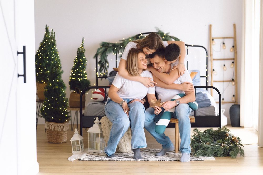 Couple in casual attire sitting on wooden floor against white wall with holiday decor and natural lighting.