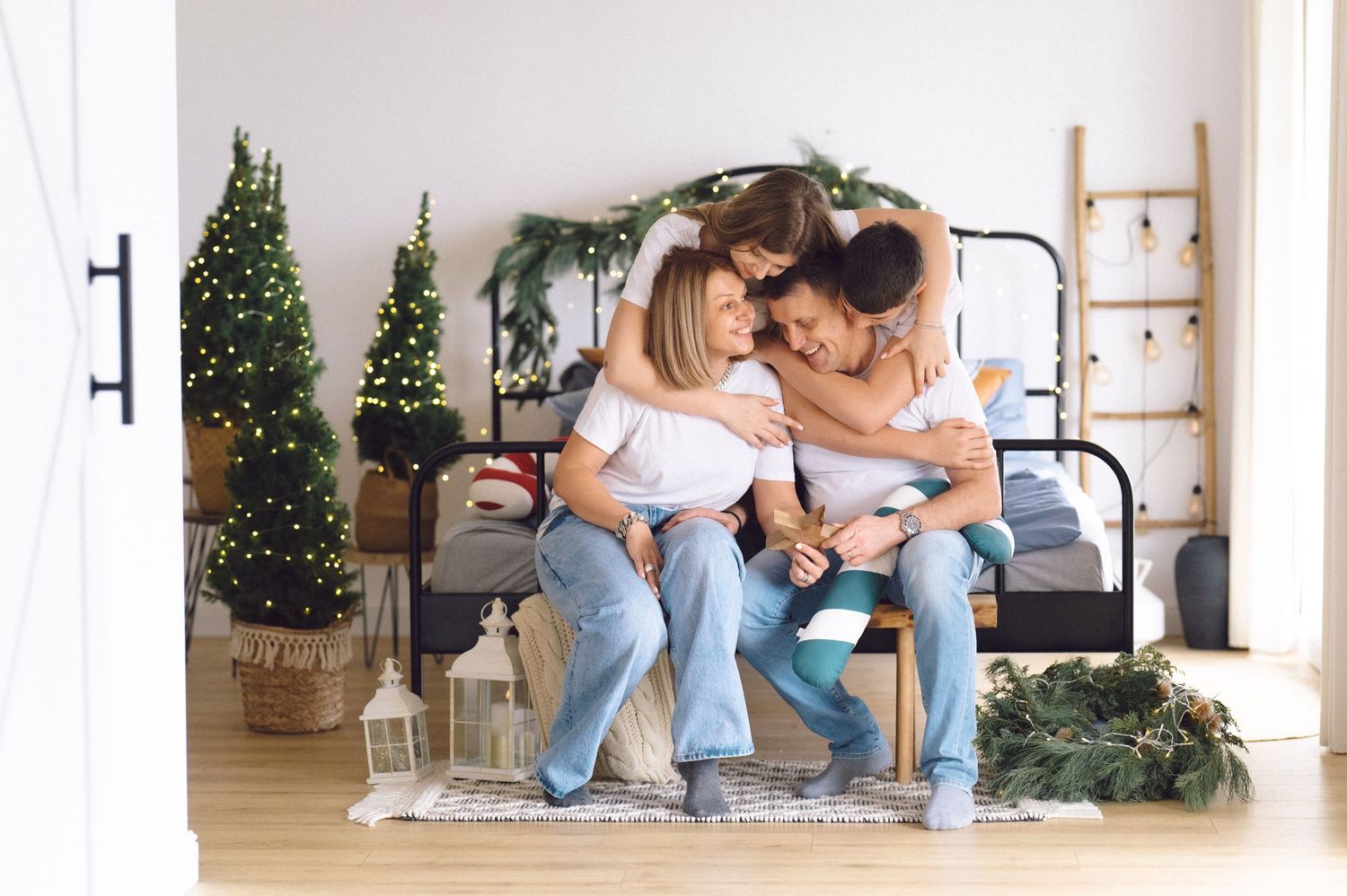Couple in casual attire sitting on wooden floor against white wall with holiday decor and natural lighting.