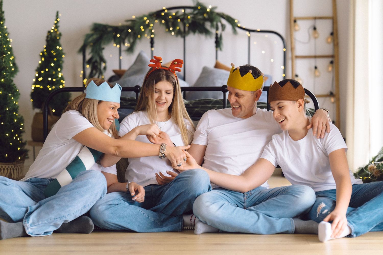 Cheerful group in casual denim outfits and holiday paper crowns sitting together on floor with festive decorations.