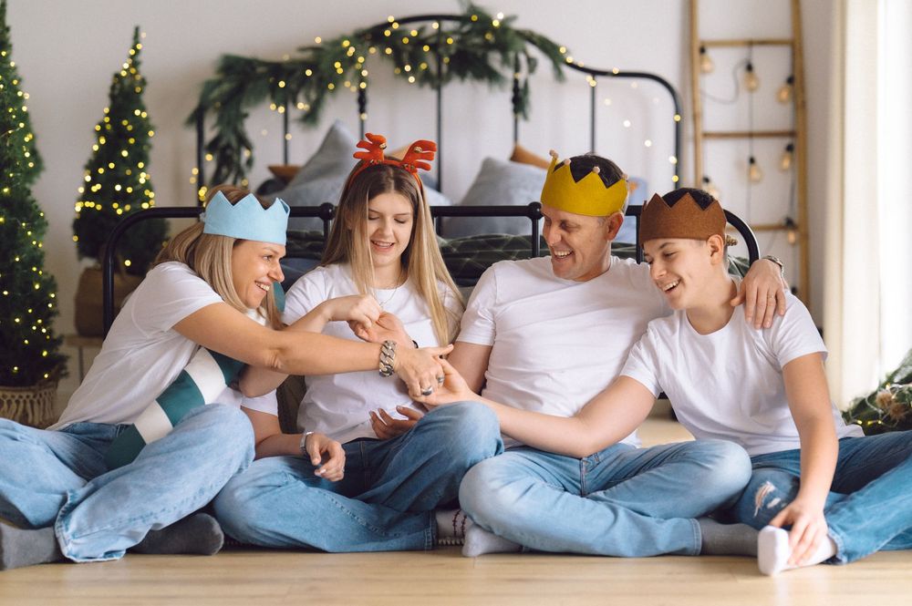 Cheerful group in casual denim outfits and holiday paper crowns sitting together on floor with festive decorations.