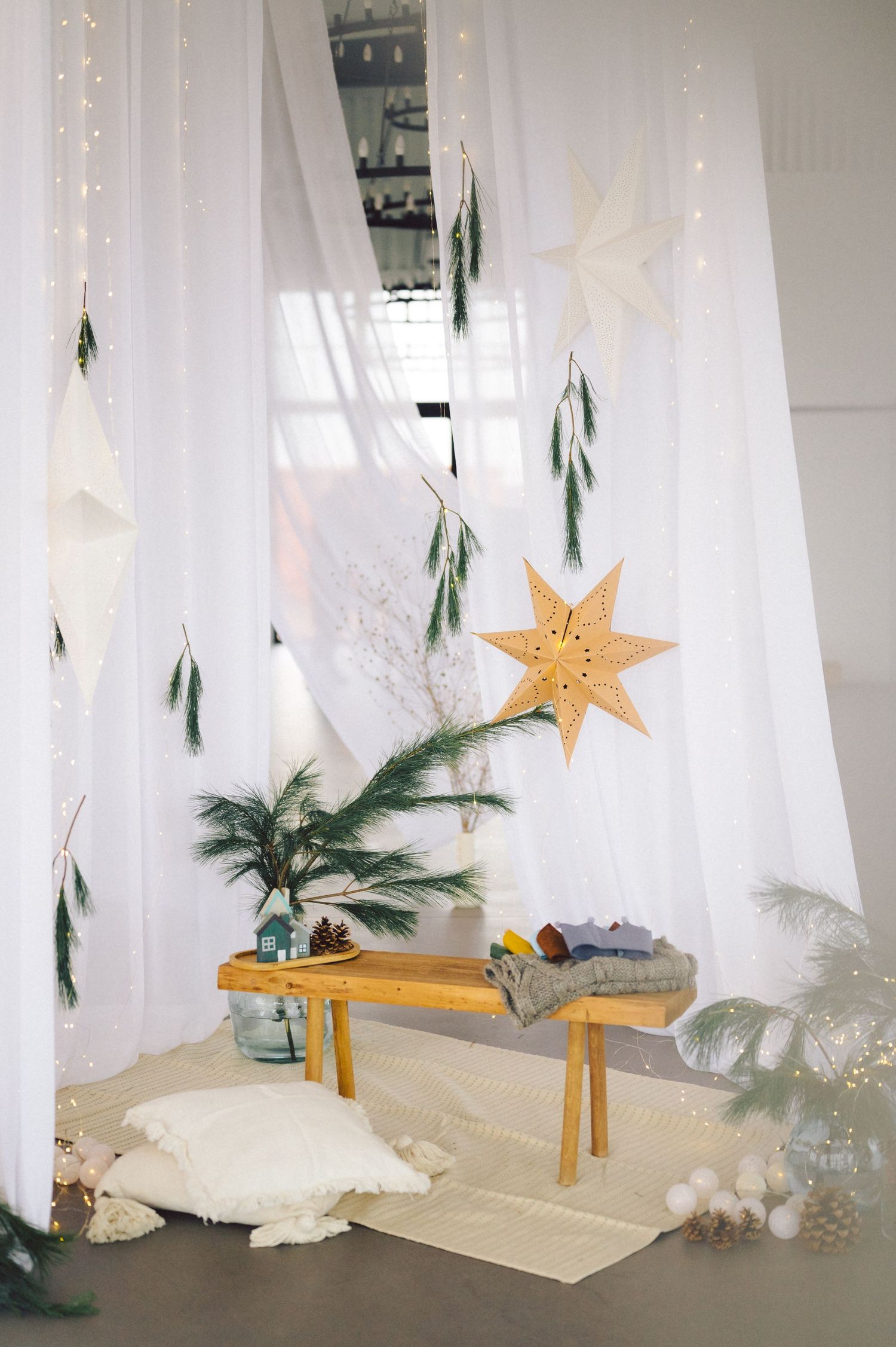 White sheer curtains create a dreamy winter wonderland setting with pine branches and gold stars as decorative elements.