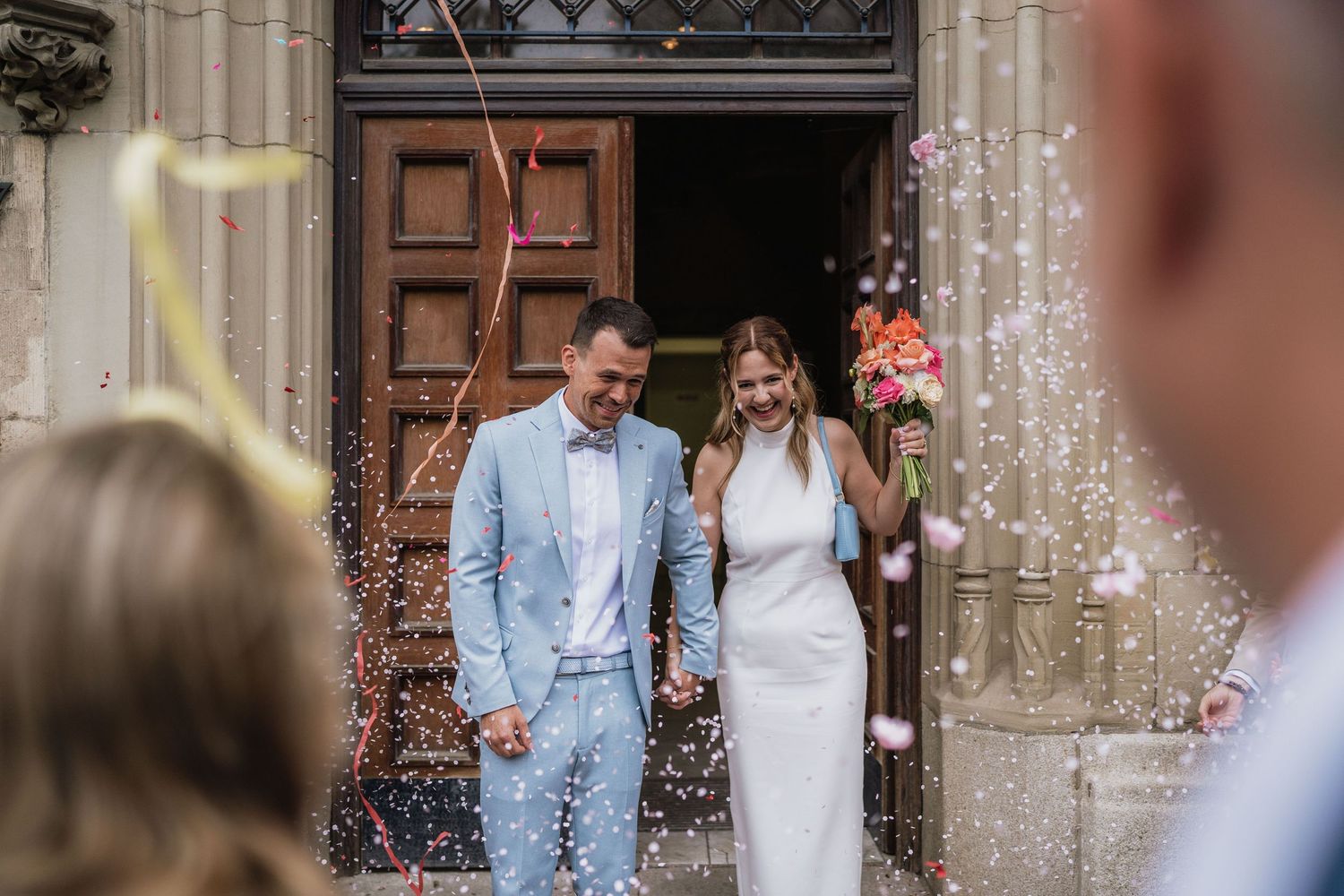 Newlyweds exit church doors while guests shower them with confetti in celebration.