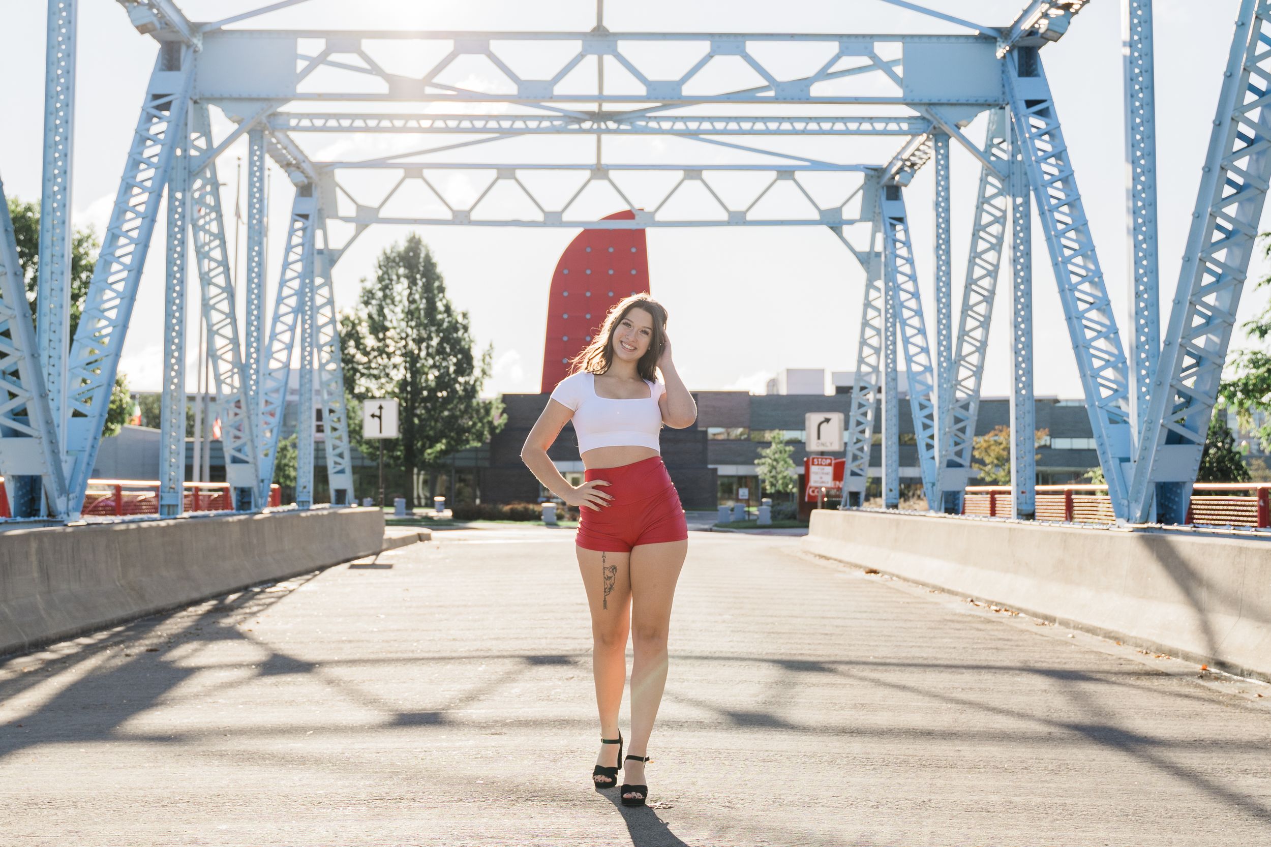 A person in red shorts and a crop top rollerblades across a blue steel bridge structure on a sunny day.