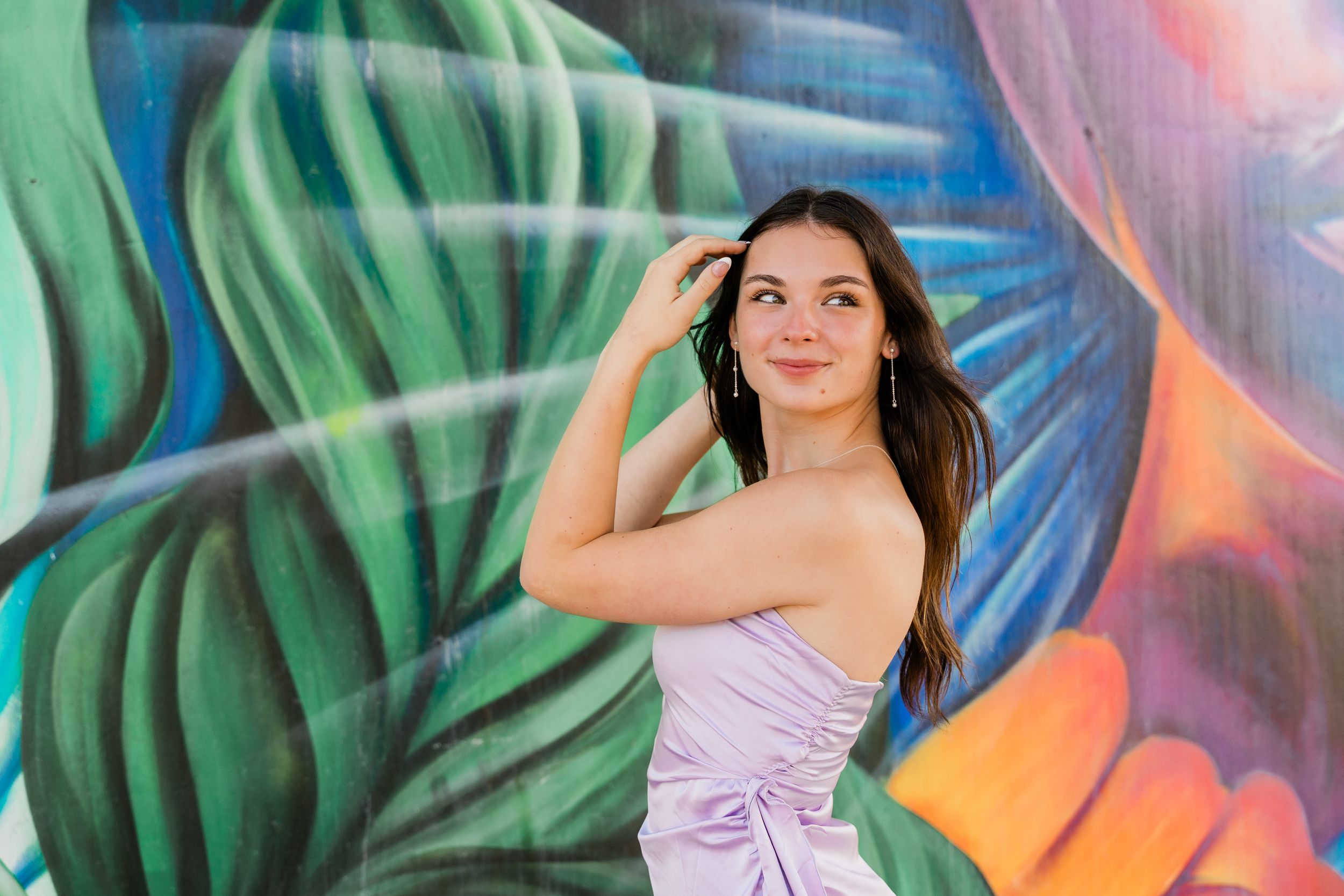 A purple dress stands out against a vibrant tropical leaf mural with blue and orange accents.
