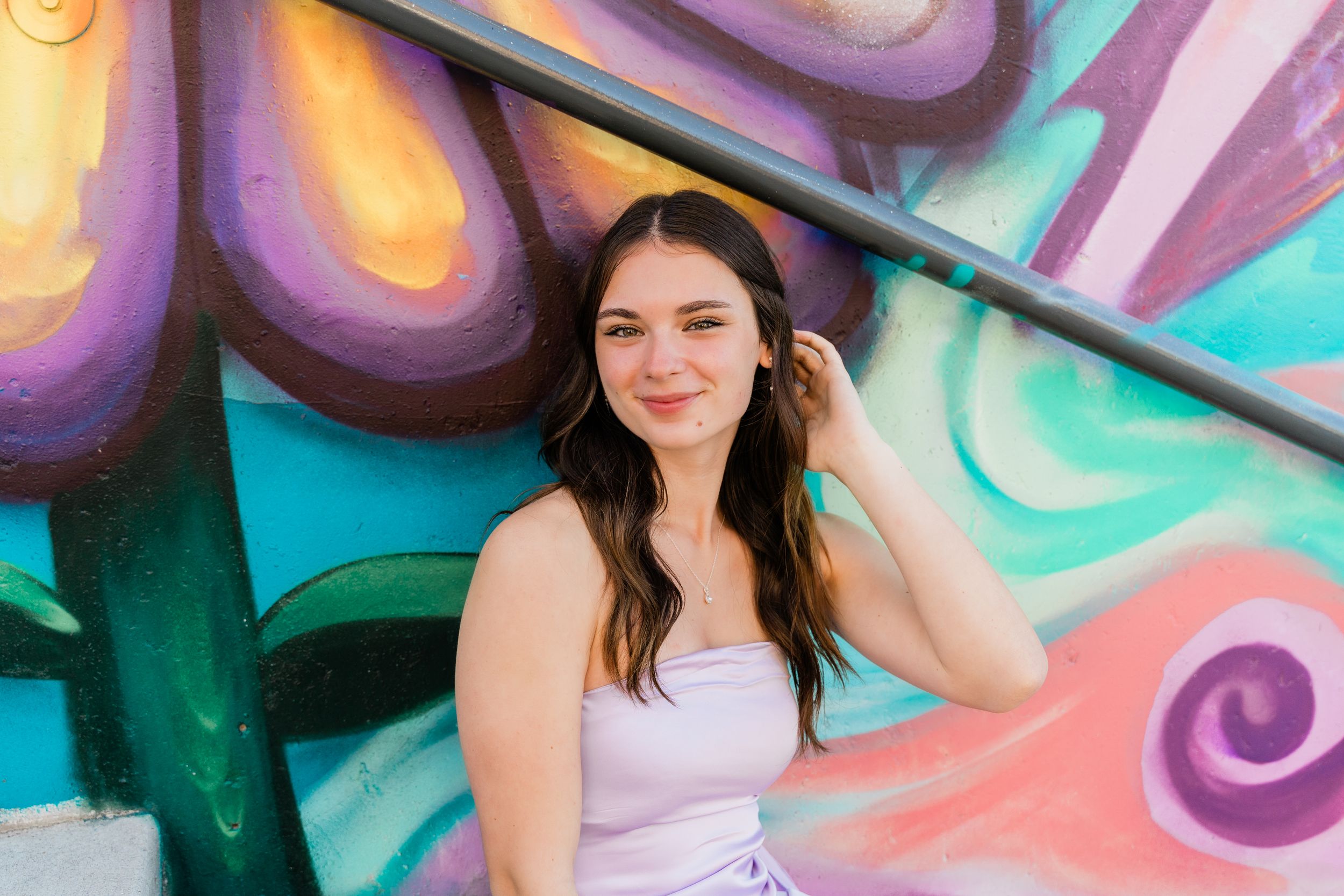 Woman in white poses against bright abstract graffiti wall with swirling purple and teal patterns.