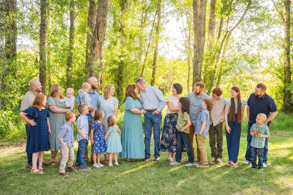 Large family group photo taken outdoors in a sunlit wooded area on a summer day.