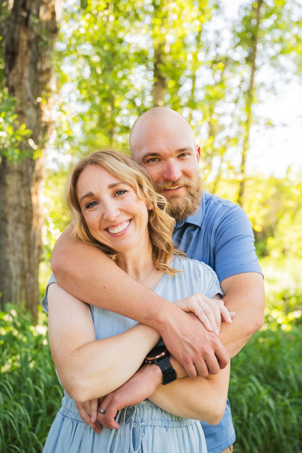 Loving couple embraces outdoors in a sun-drenched forest setting with lush greenery and natural backlight.