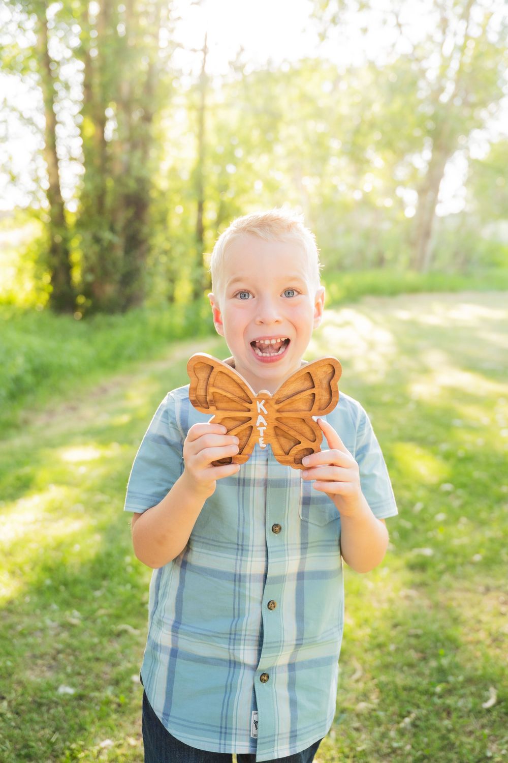 A joyful child holds up a decorative wooden butterfly cutout in a sunlit forest setting.