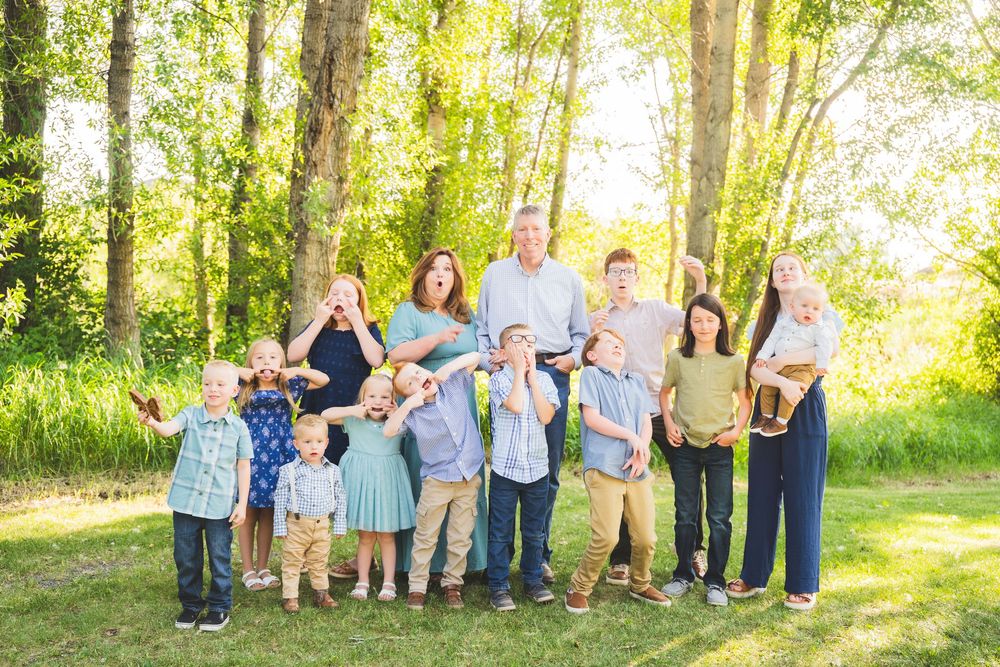Extended family gathering posed together among trees with golden sunlight filtering through the leaves.