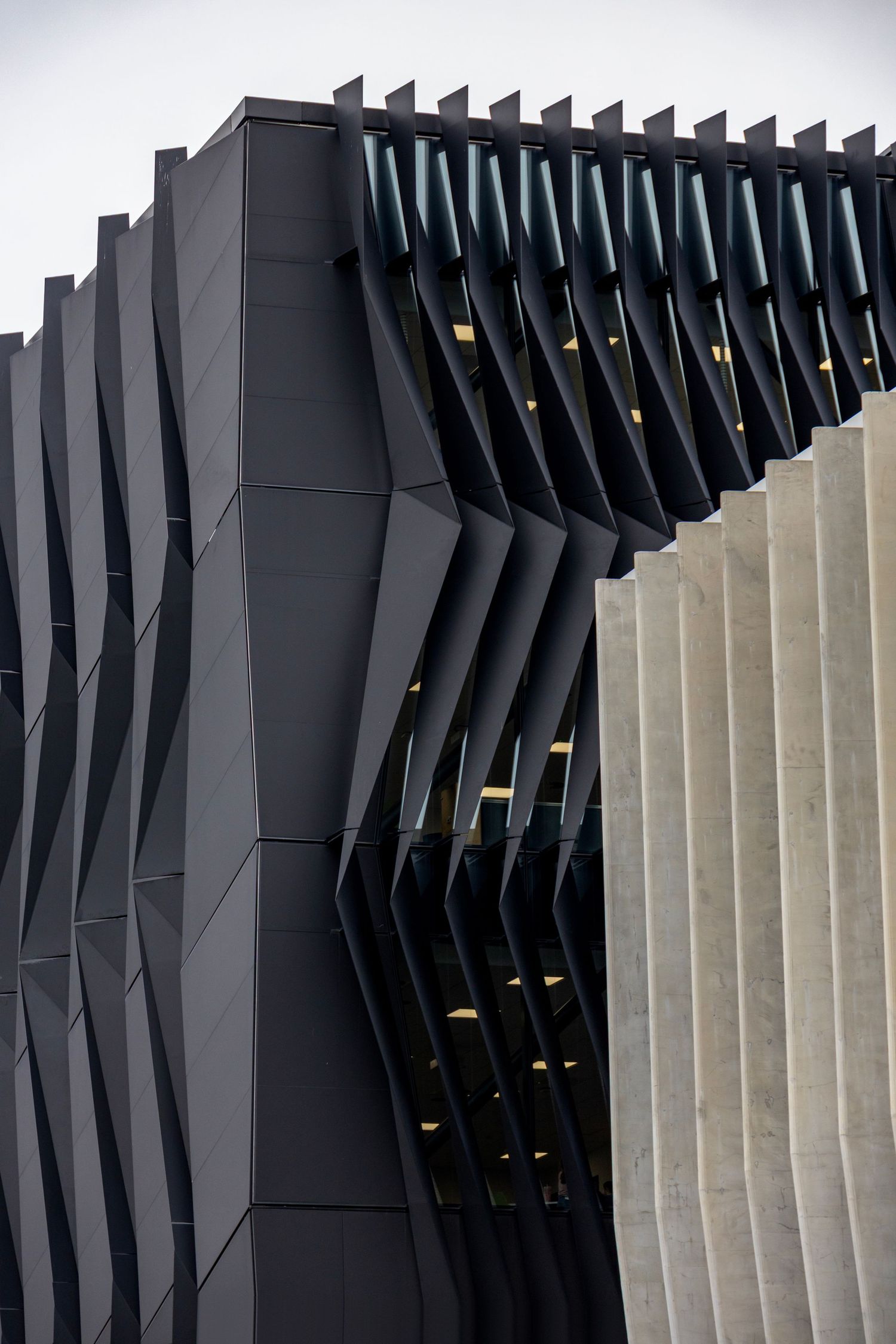 A dramatic black-finned facade curves toward a textured concrete wall under soft daylight.