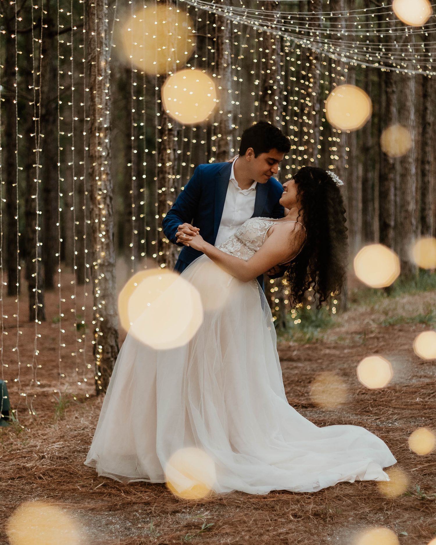 Wedding couple dances in a romantic forest setting with twinkling string lights creating a magical atmosphere.