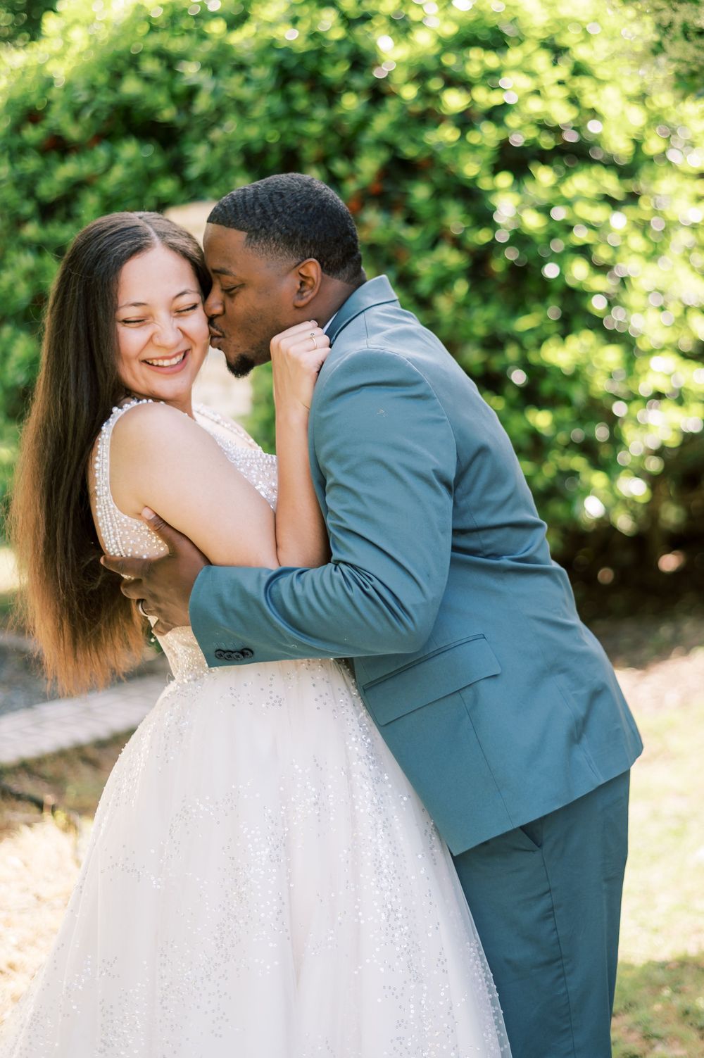 A romantic garden wedding moment with a couple embracing in formal attire under natural sunlight and greenery.