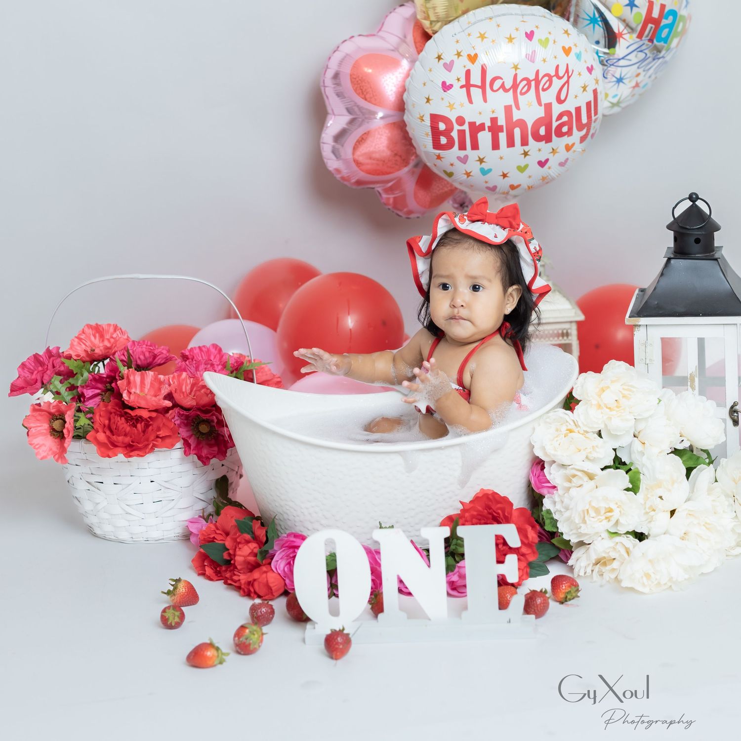 Pretty pink and white floral birthday cake smash setup with balloons, flowers, and 'ONE' letters for milestone celebration.