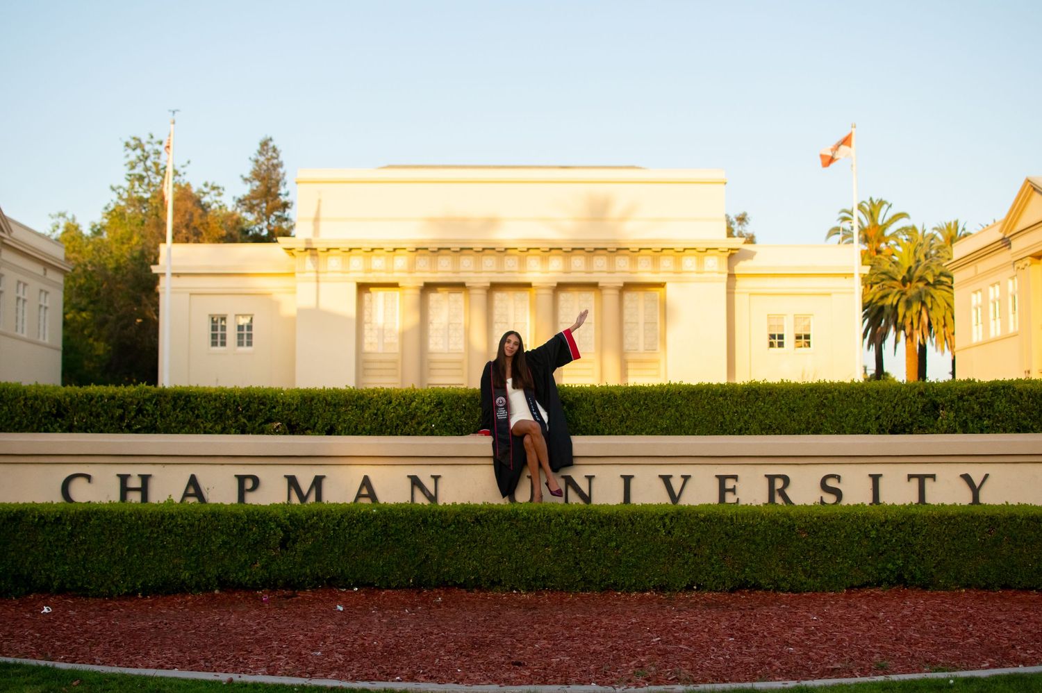 Graduate celebrating in cap and gown in front of Chapman University sign at golden hour.