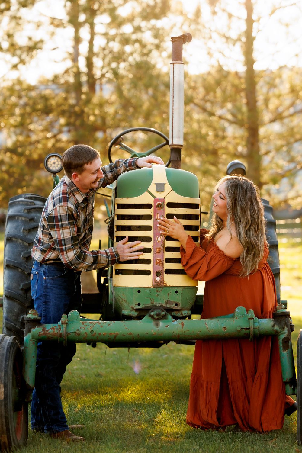 A couple shares a romantic moment on a vintage green tractor during sunset in a grassy field.