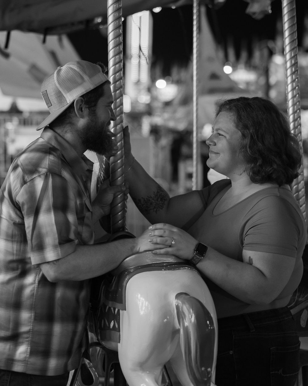 A couple shares an intimate moment while riding on a carousel horse in this black and white photograph.
