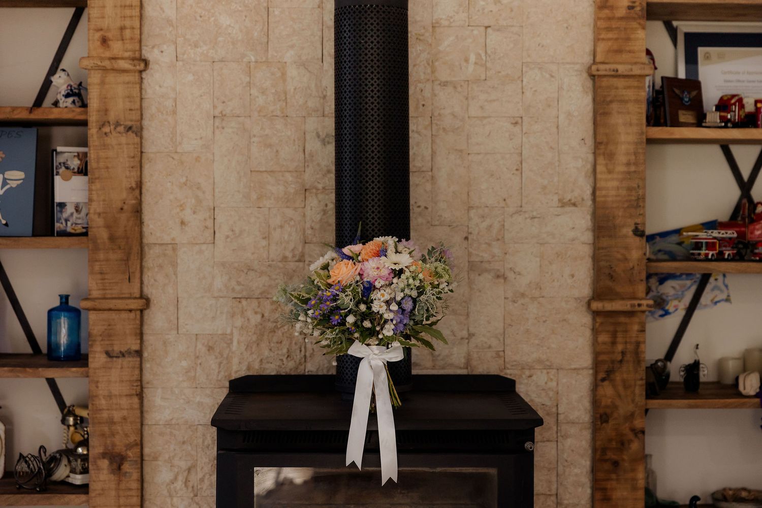 A romantic bridal bouquet with pink and white flowers rests on a black surface against a stone wall with rustic wooden beams.