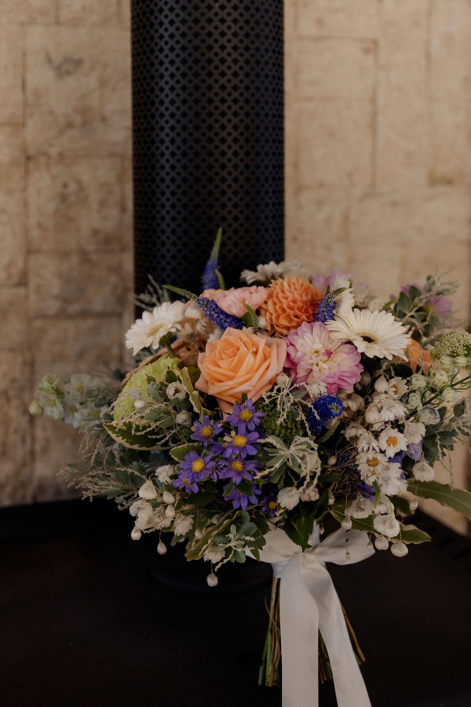 Rustic bridal bouquet featuring peach roses, white and purple wildflowers against a textured dark backdrop.