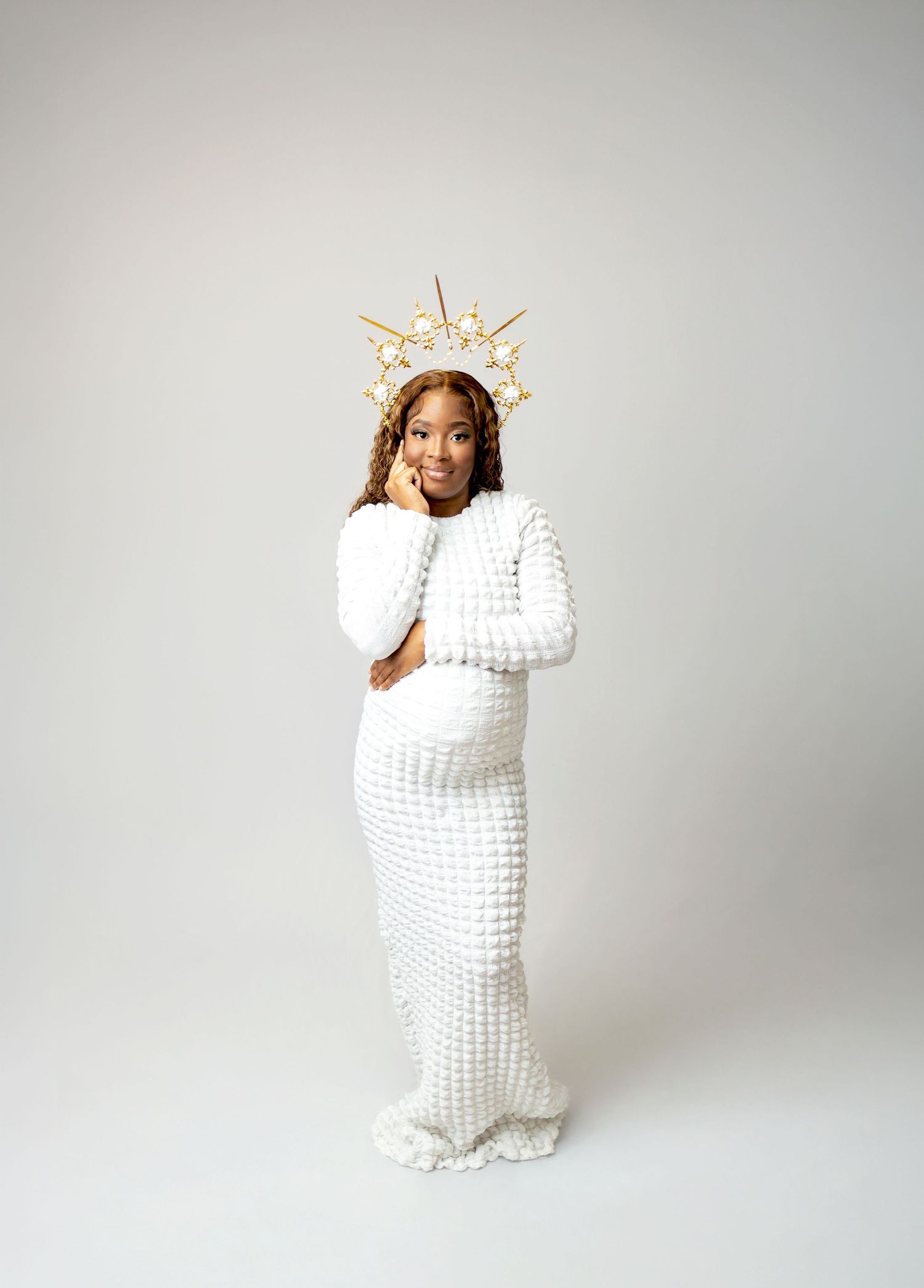 A figure in a flowing navy dress stands near woven baskets and circular wall decor in a rustic interior setting.