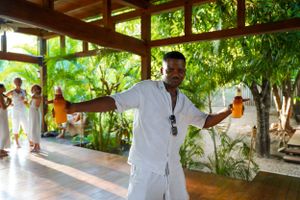 Staff member in white uniform welcoming guests in tropical resort setting.
