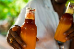 Close-up of hand holding brown glass bottle against blurred background.