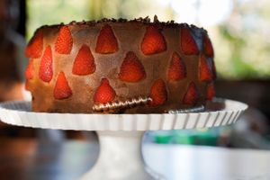 Chocolate cake decorated with fresh strawberries displayed on white cake stand.