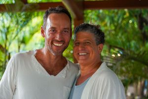 Two men in white shirts sharing genuine laughter during a sunny outdoor gathering.